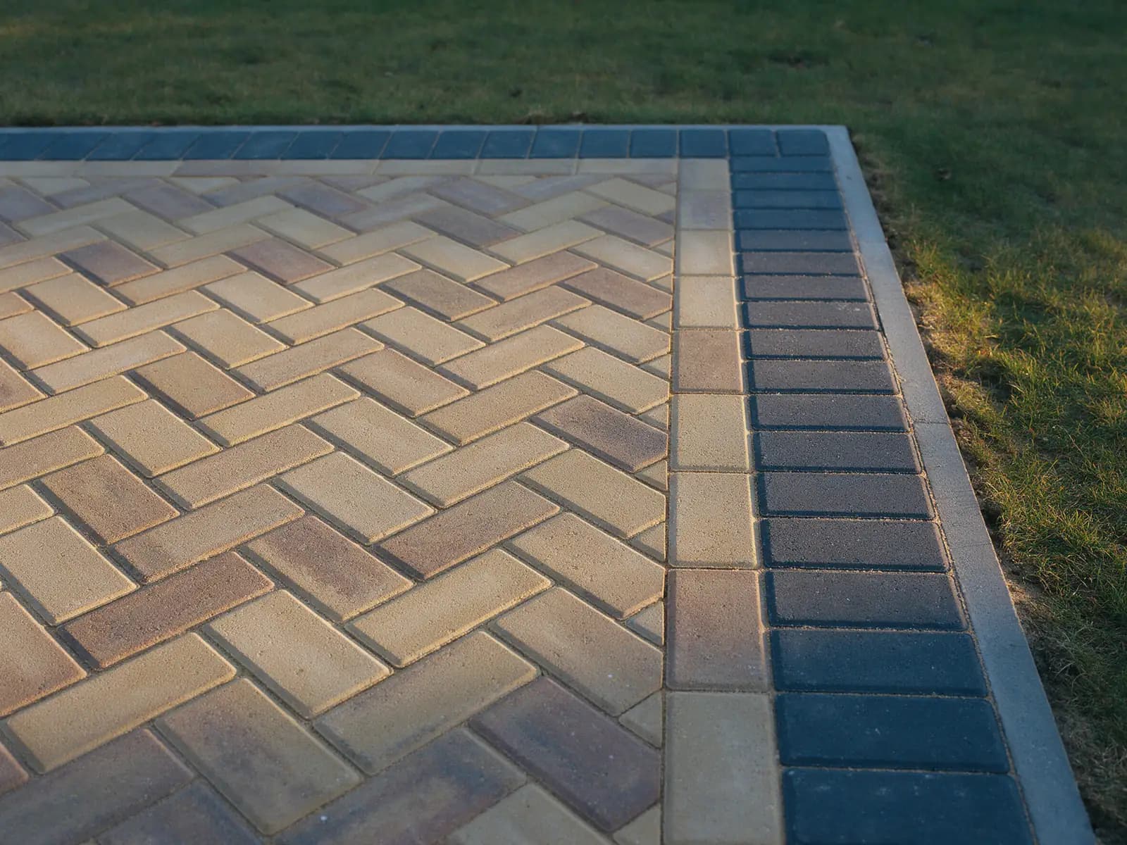 Herringbone block paving meeting a charcoal edging course on a newly laid driveway